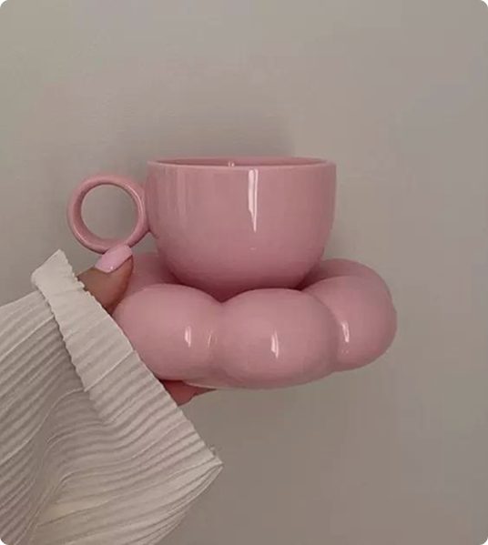 A pink cup on a cloud-shaped saucer, held in hand